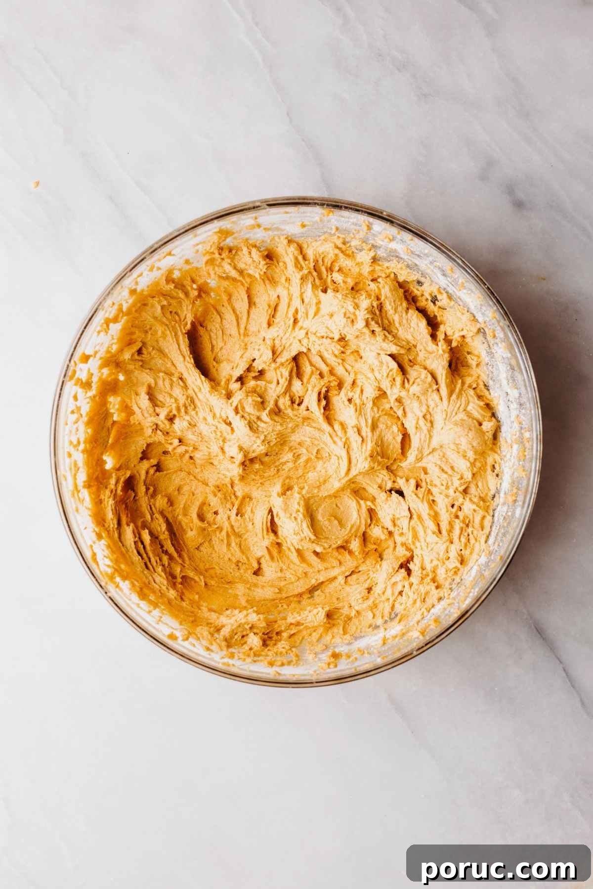 Pumpkin whoopie pie batter in a large glass mixing bowl on a light grey marbled background.