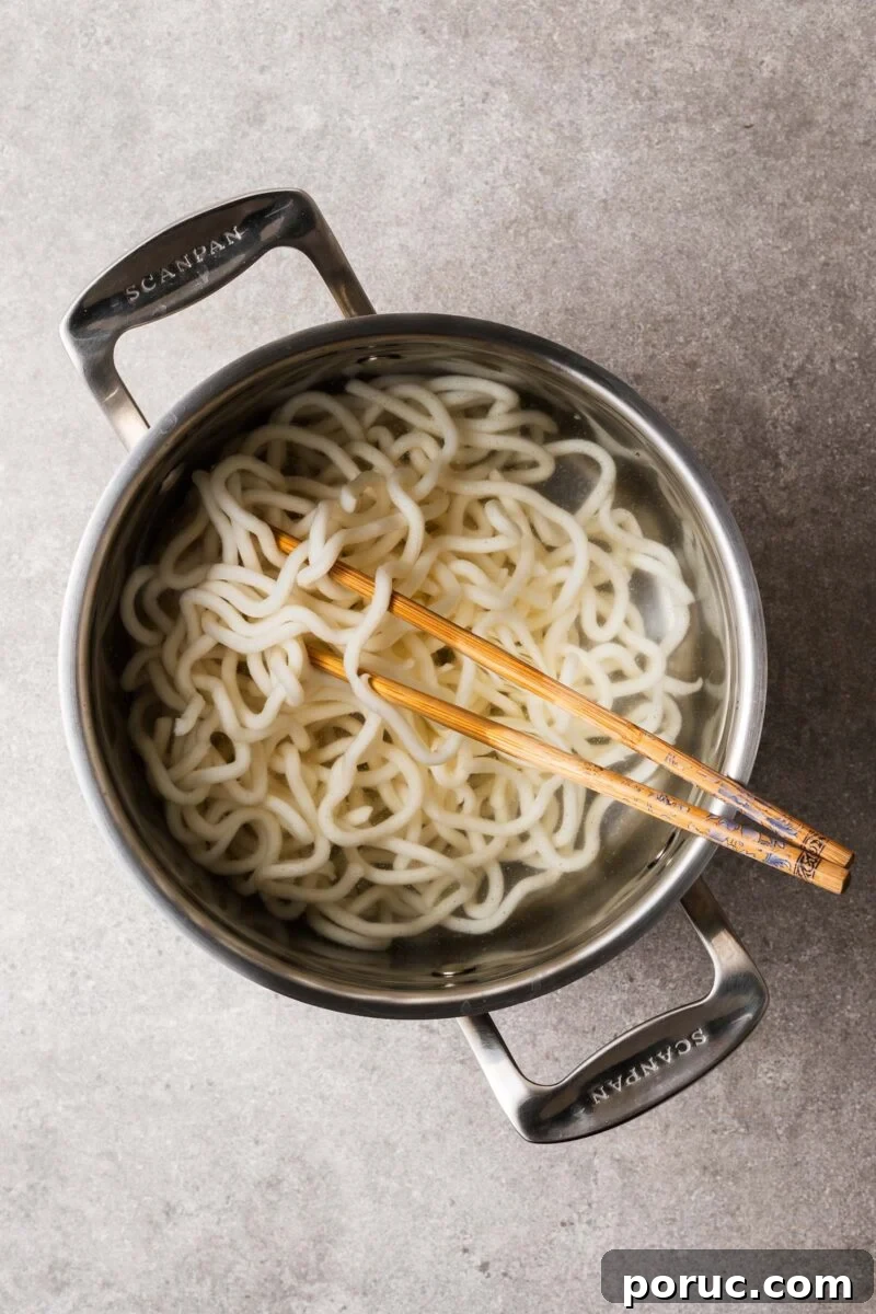 Kake Udon: Classic Japanese Broth Noodle Soup Recipe 5 Udon noodles in a large pot being separated with chopsticks.