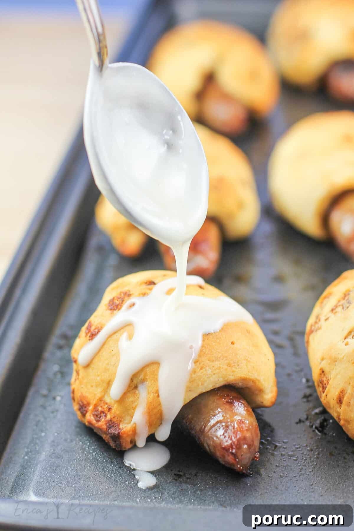 Cinnamon Roll Pig in a Blanket Bites: Sweet Savory Appetizer 2 cinnamon roll pigs in a blanket on metal bake sheet; spoon is drizzling icing over top