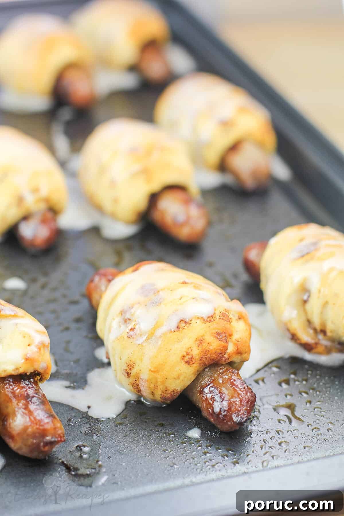 Cinnamon Roll Pig in a Blanket Bites: Sweet Savory Appetizer 8 breakfast pigs in a blanket on metal bake sheet topped with icing