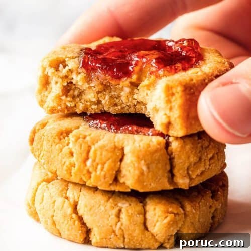 Peanut Butter and Jelly Cookies Recipe — Classic Sandwich Twist 6 Three jam thumbprint cookies stacked with a bite taken from the top one.
