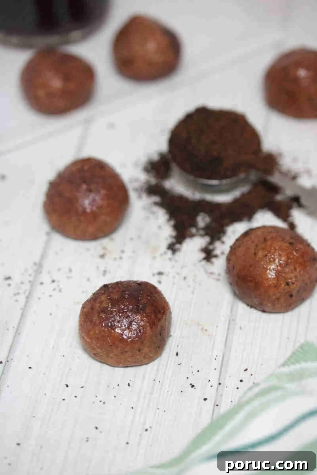 Gluten-Free Coffee Protein Bites: Energy Snacks for Busy Mornings 2 Coffee protein balls covered in cocoa powder with a spoon of coffee grinds beside them.