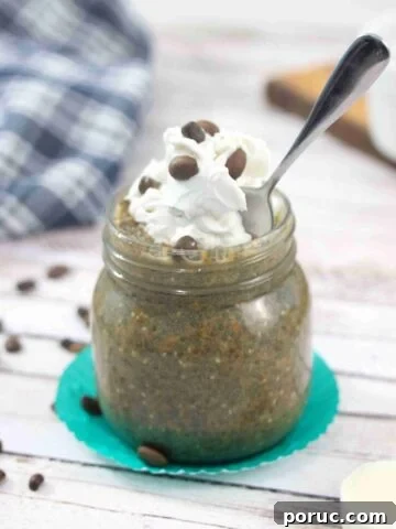 Mason jar with coffee chia pudding topped with dairy-free whipped cream and a spoon in the jar.