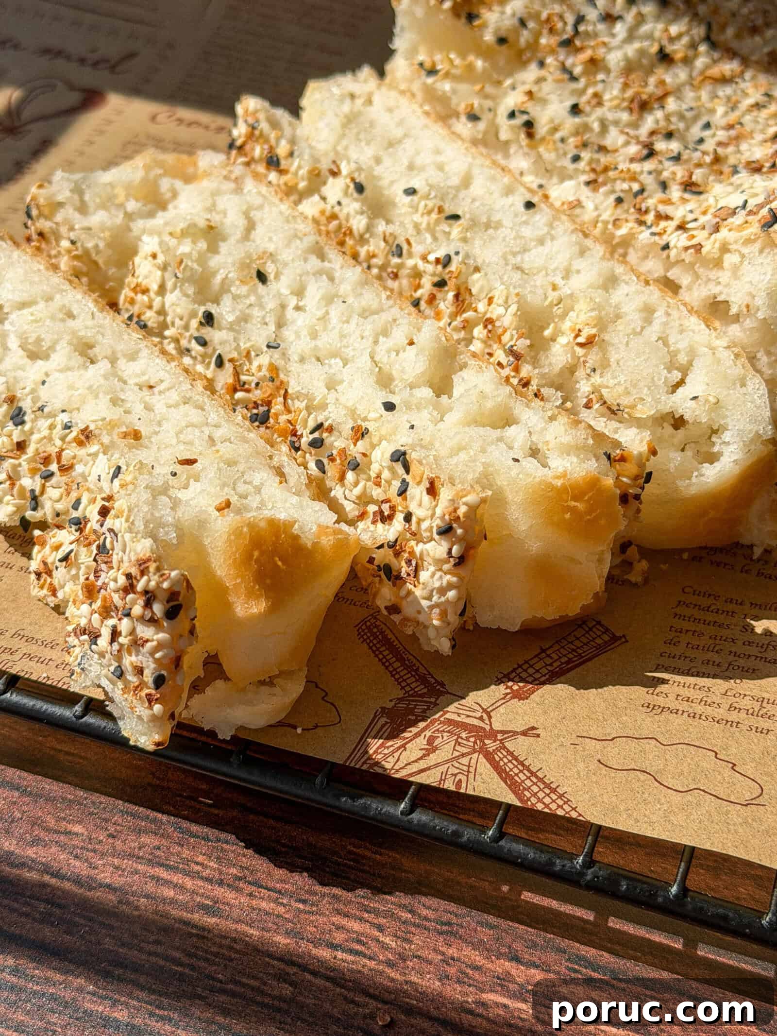 Viral Blender Rice Bread Recipe — Gluten-Free, No Flour 3 Sliced Viral Blender Rice Bread topped with a mix of sesame seeds and seasoning sits on parchment paper printed with drawings, including a windmill, on a wire cooling rack in sunlight.