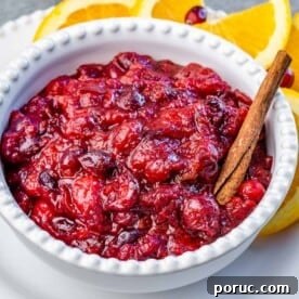 Tangy Cranberry Orange Sauce Recipe for Holidays and Leftovers 10 A white bowl filled with cranberry sauce with a cinnamon stick in bowl.