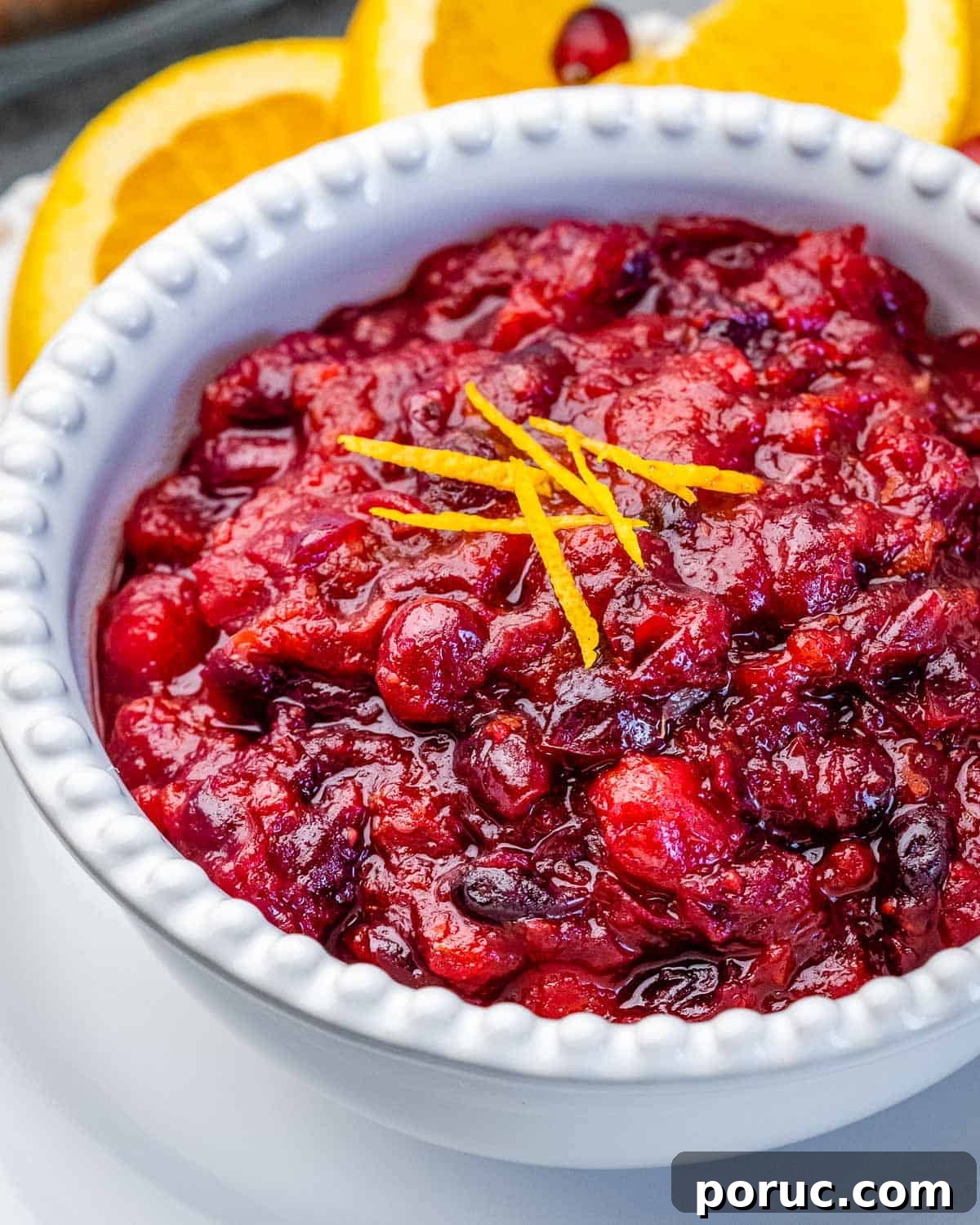 Tangy Cranberry Orange Sauce Recipe for Holidays and Leftovers 7 A white bowl with cranberry sauce topped with orange peel garnish.