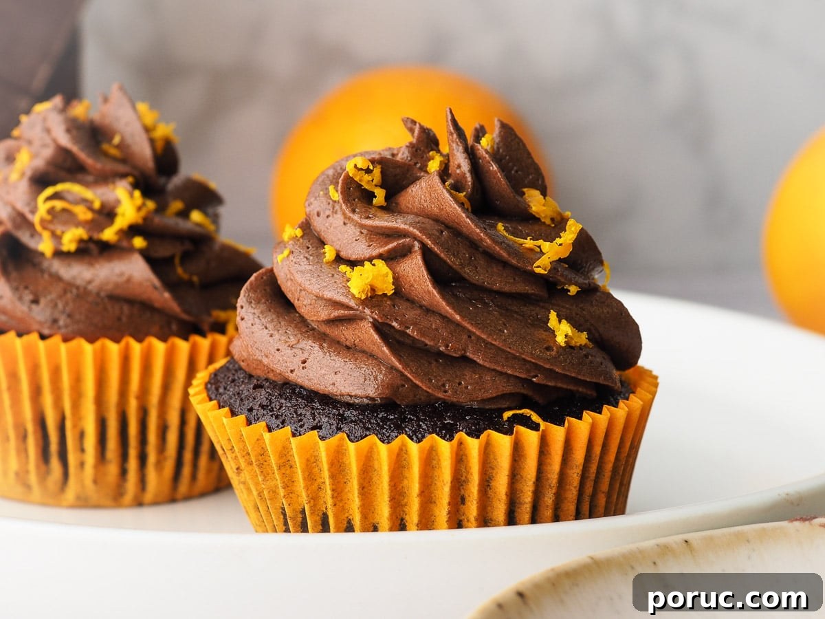 Chocolate Orange Cupcakes with Zesty Orange Glaze 2 Cupcakes on a plate with fresh oranges in the background.