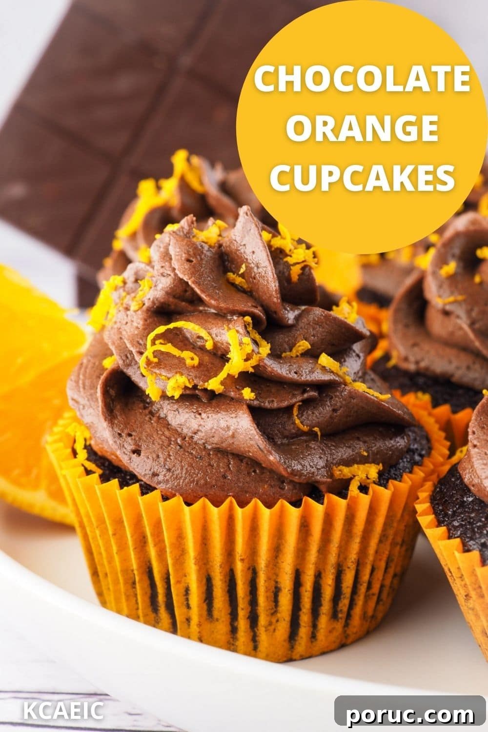 Chocolate Orange Cupcakes with Zesty Orange Glaze 10 Cupcakes on a plate with fresh oranges and chocolate in the background, with text overlay chocolate orange cupcakes and KCAEIC.