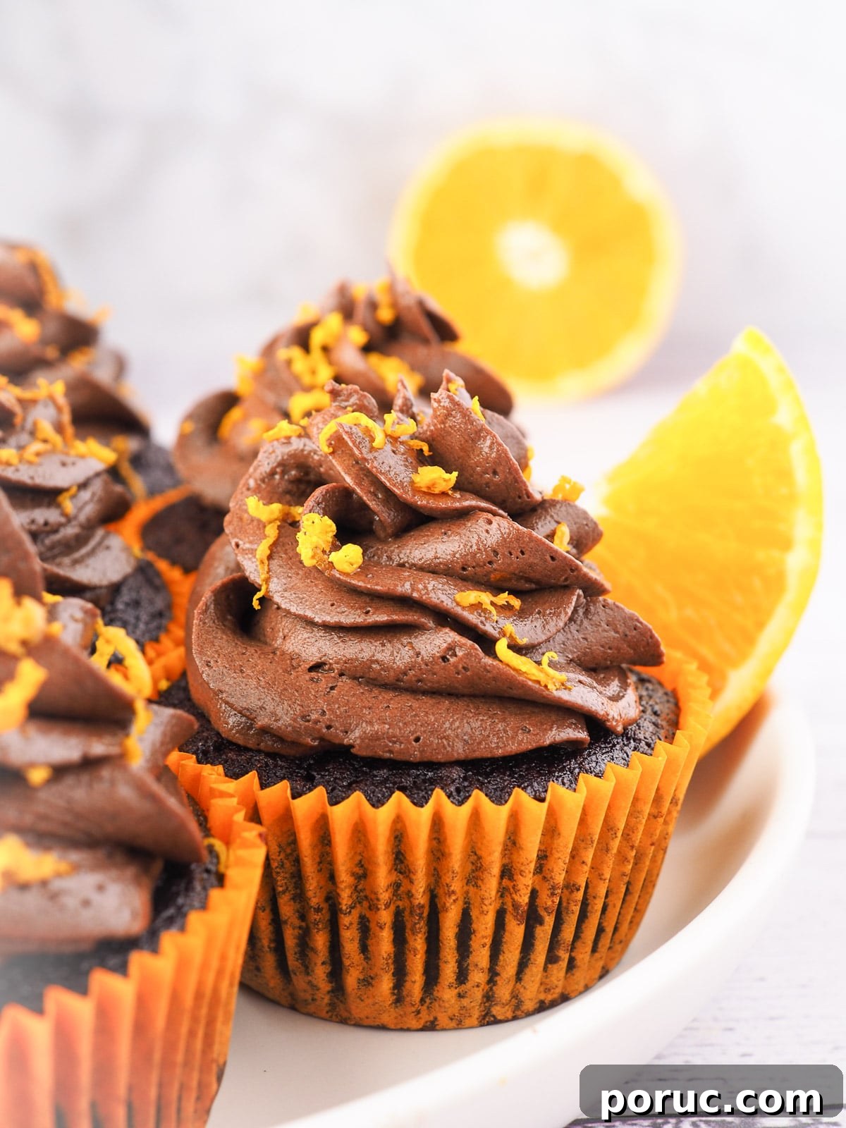 Chocolate Orange Cupcakes with Zesty Orange Glaze 11 Cupcakes on a plate with fresh oranges in the background.
