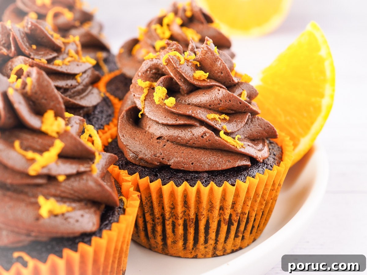 Chocolate Orange Cupcakes with Zesty Orange Glaze 8 Cupcakes on a plate with chocolate and fresh oranges in the background.