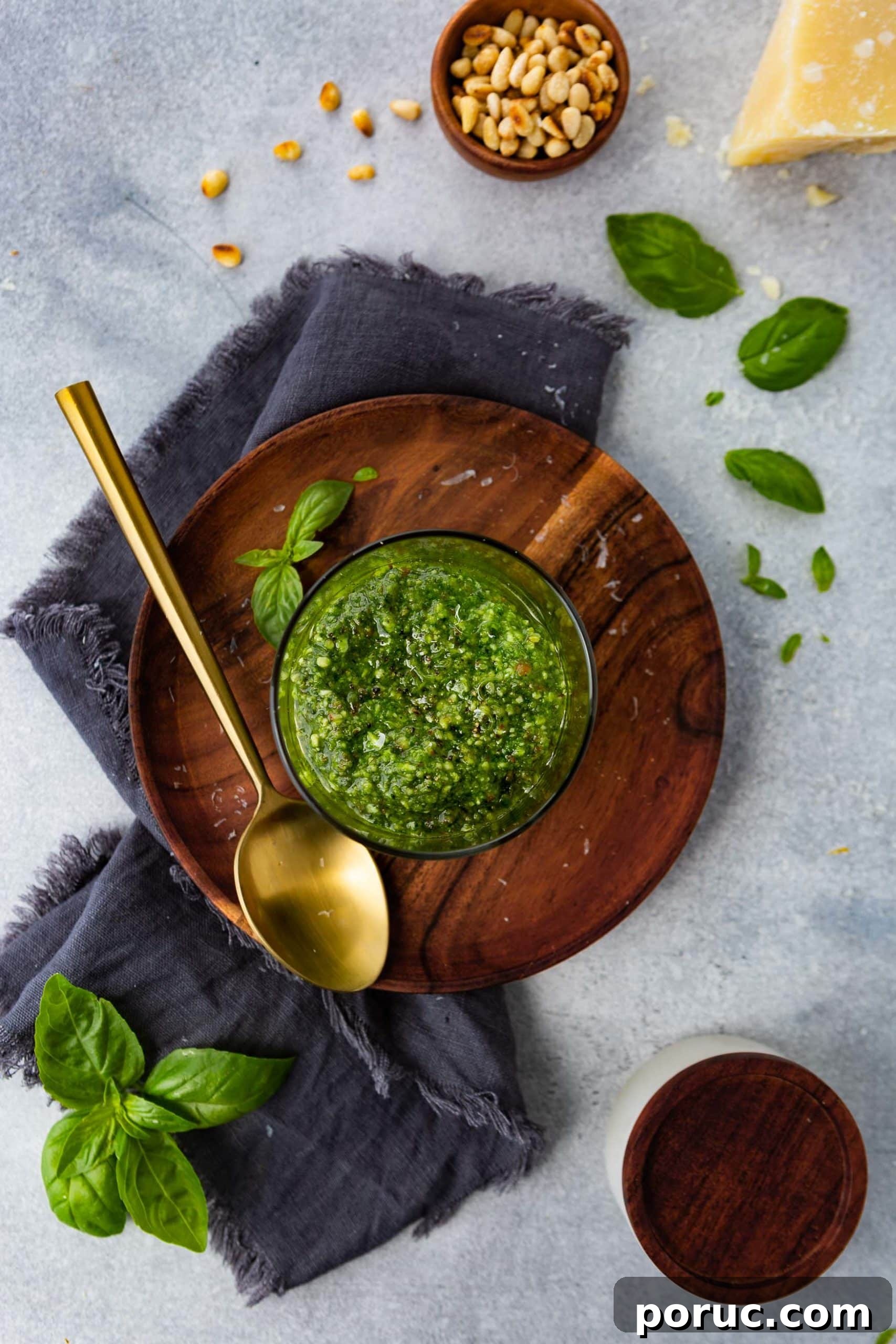 Homemade Classic Basil Pesto Recipe for Pasta & Sandwiches 5 a photo of a jar of homemade pesto sauce on a wooden plate with a gold spoon next to it.