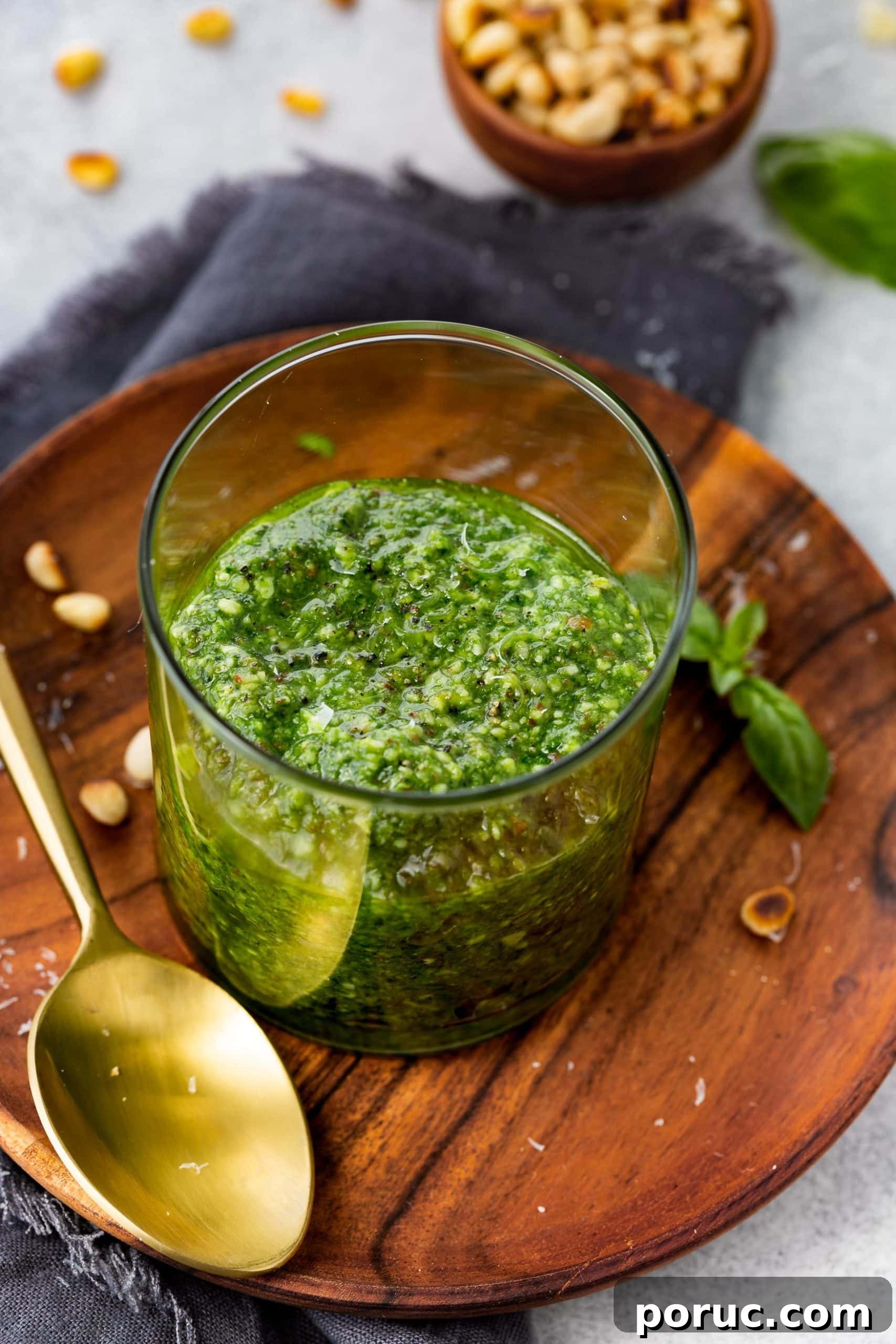 Homemade Classic Basil Pesto Recipe for Pasta & Sandwiches 6 a photo of a glass jar of homemade pesto sauce on a wooden plate with a gold spoon laying next to the jar.