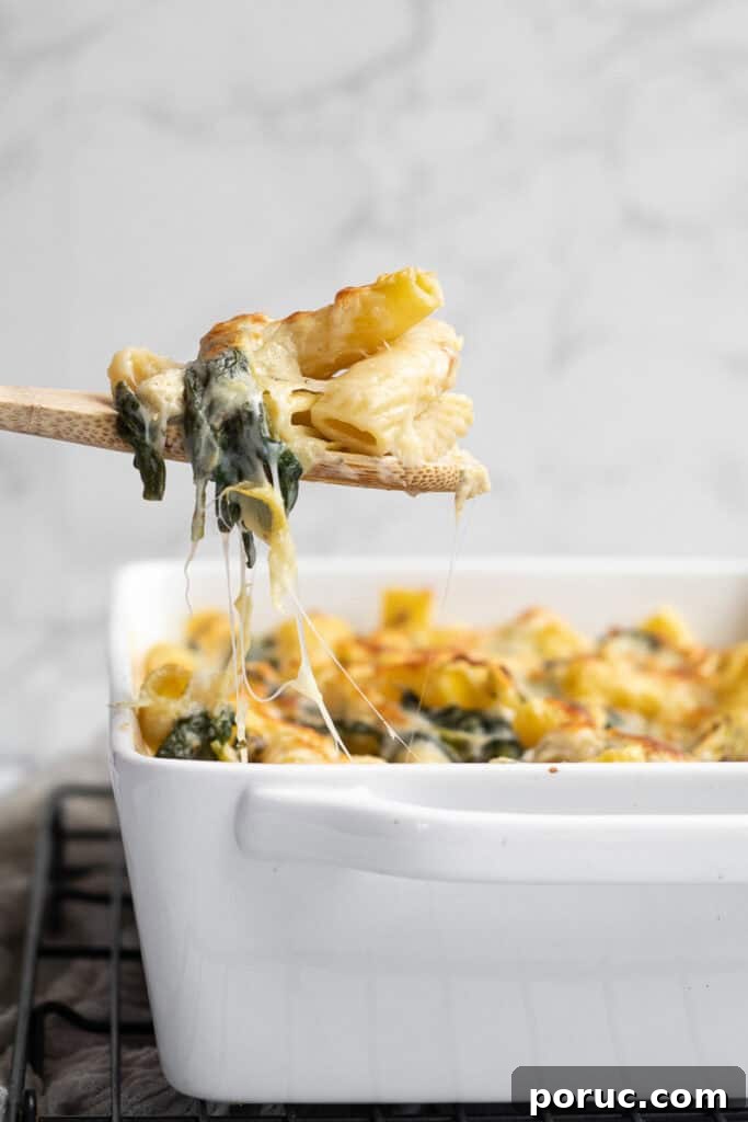 Spinach and Artichoke Pasta Bake with 7 Simple Ingredients 3 pasta on a wooden serving spoon with a cheese pull.