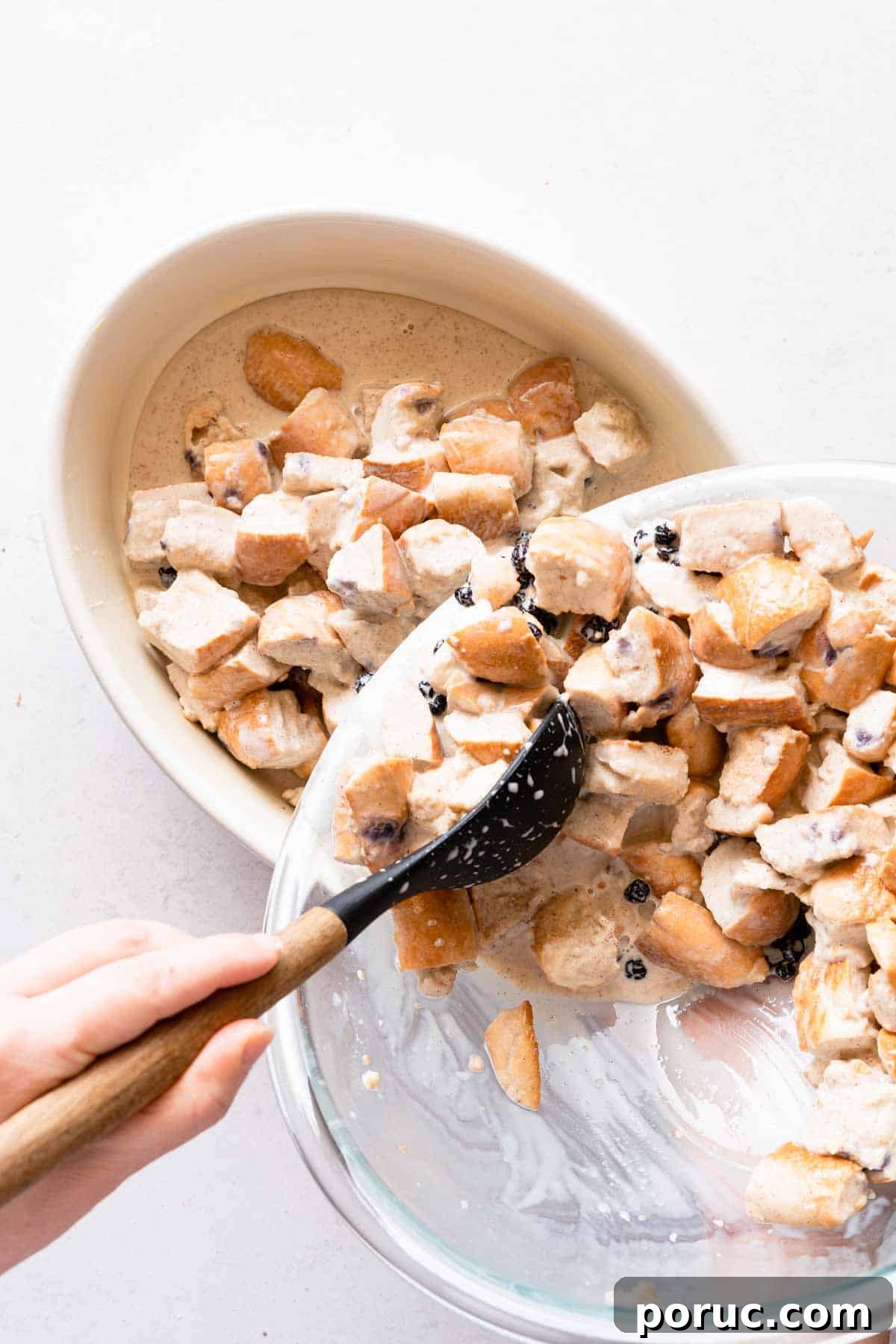 spoon scooping bread pudding mix from bowl into oval casserole dish.