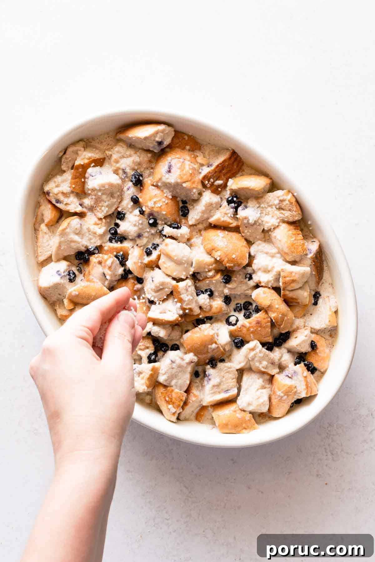 hand sprinkling sugar overtop bread pudding before baking.