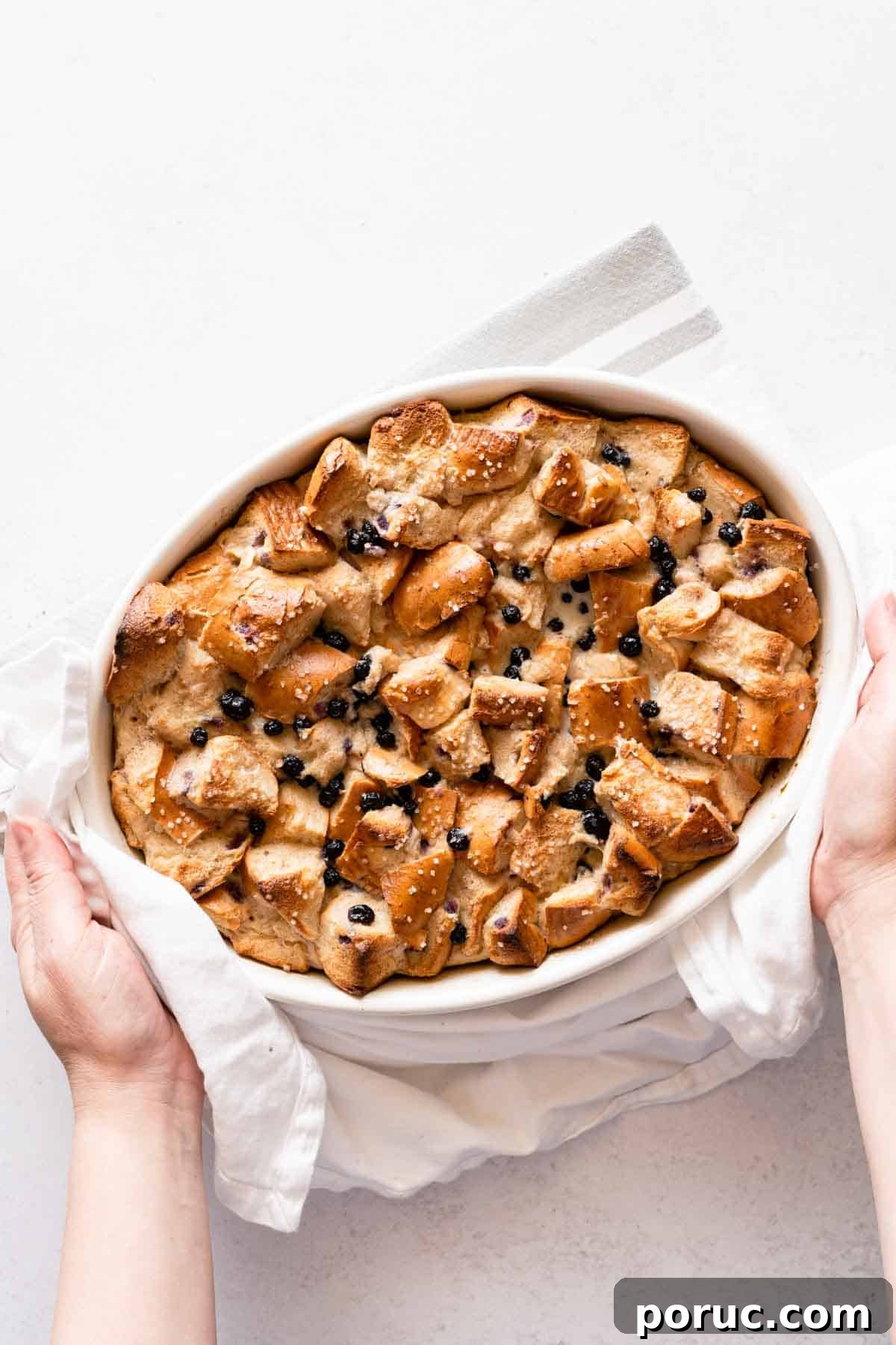 hands holding bread pudding in oval casserole dish after baking.