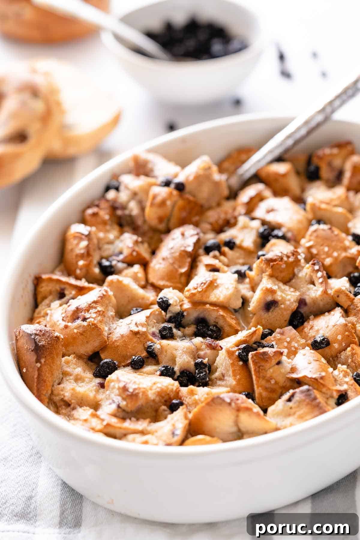 bread pudding made with bagels in white casserole dish with spoon.