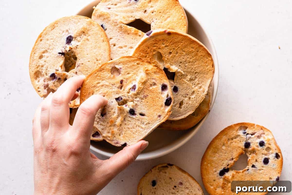 hand holding toasted bagel overtop bowl of other toasted bagel halves.