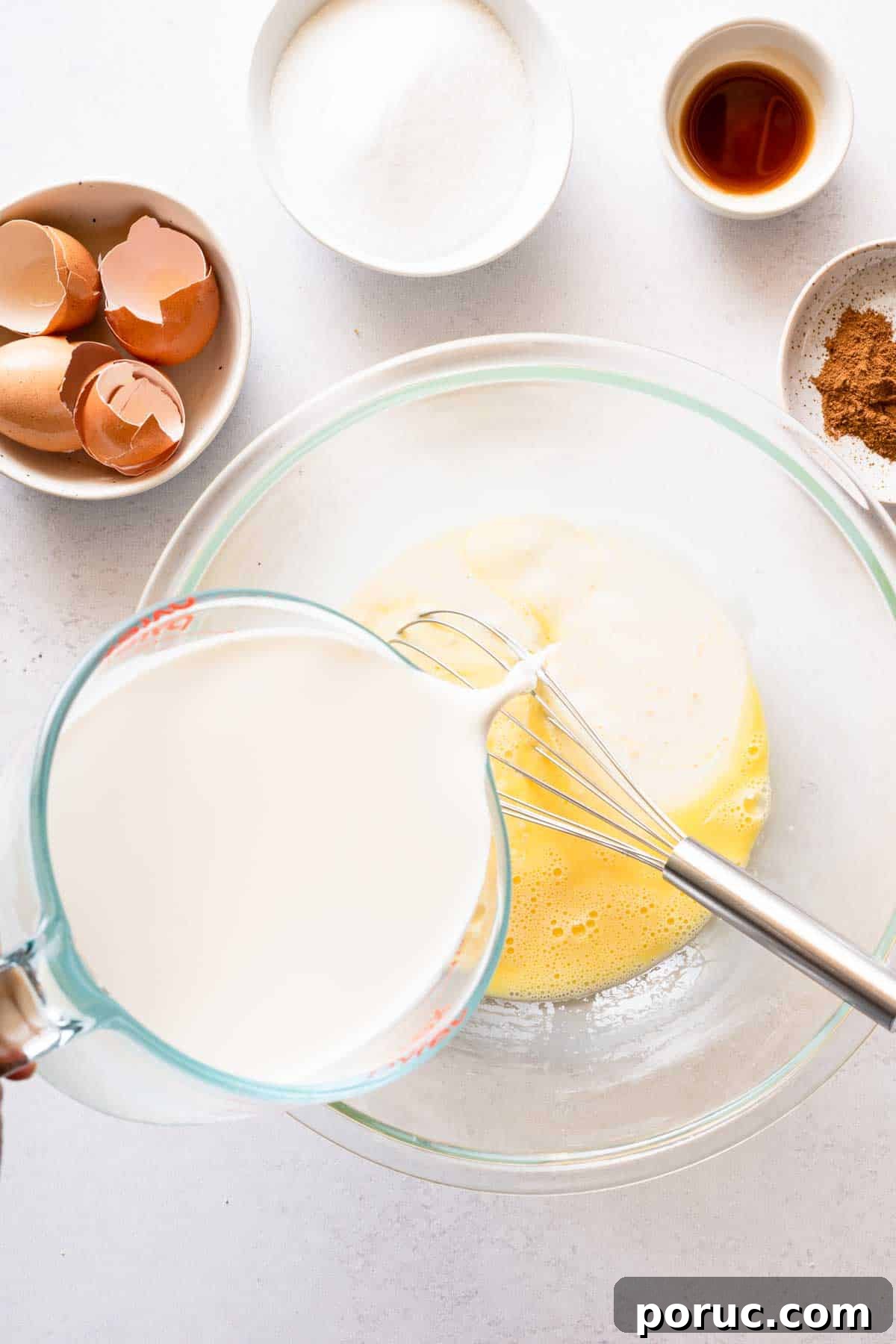 half and half being poured from measuring cup into bowl of whisked eggs.