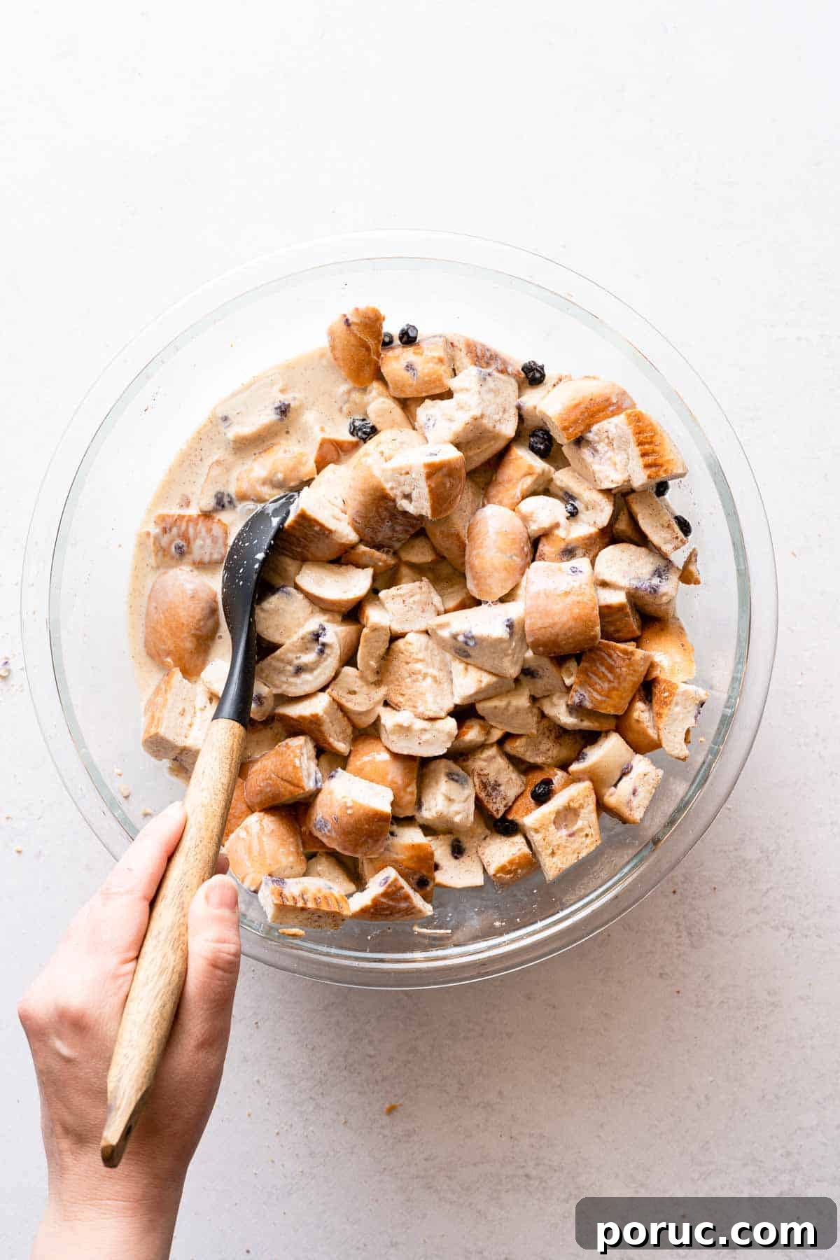 bread pudding mix in glass bowl being stirred with large spoon.