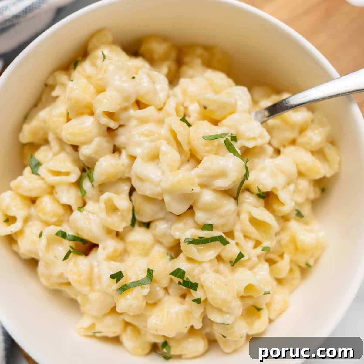 A bowl of creamy macaroni and cheese topped with chopped herbs, with a fork resting inside.