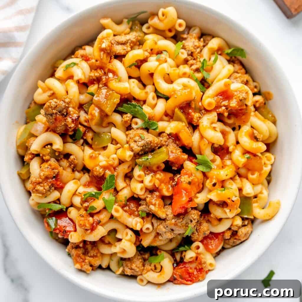 A bowl filled with macaroni pasta mixed with ground meat, diced tomatoes, green bell peppers, and garnished with parsley.
