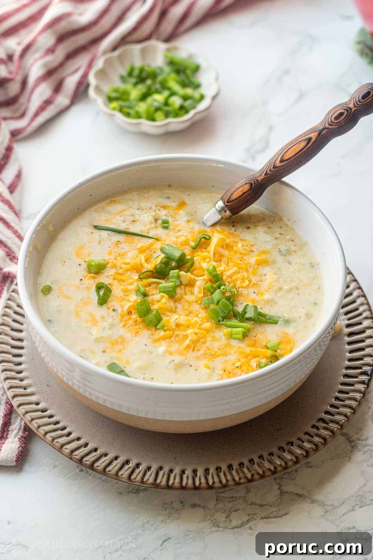 Creamy Potato, Leek & Cauliflower Soup Recipe 2 Bowl of cooked cauliflower leek potato soup on plate with wooden spoon.