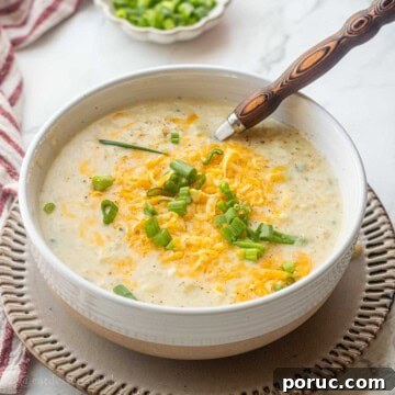 Creamy Potato, Leek & Cauliflower Soup Recipe 15 Bowl of cooked cauliflower leek potato soup on plate with wooden spoon.