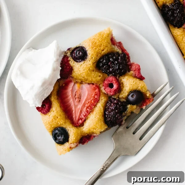 A slice of berry sheet cake on a white plate with fork and dollop of cream.