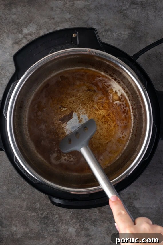 A spatula is used to scrape the browned bits from the bottom of the instant pot after deglazing with broth.