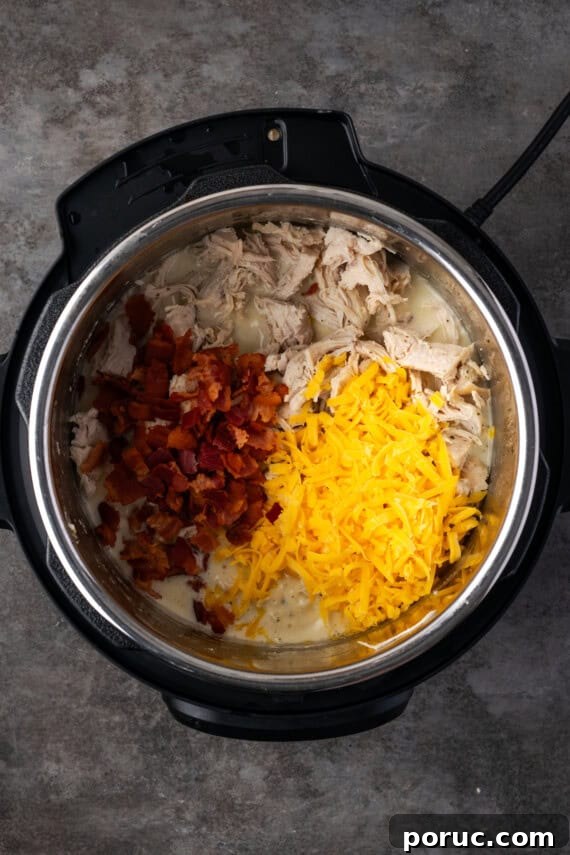 Shredded chicken, diced bacon, and shredded cheese added to the cream cheese sauce inside the instant pot.