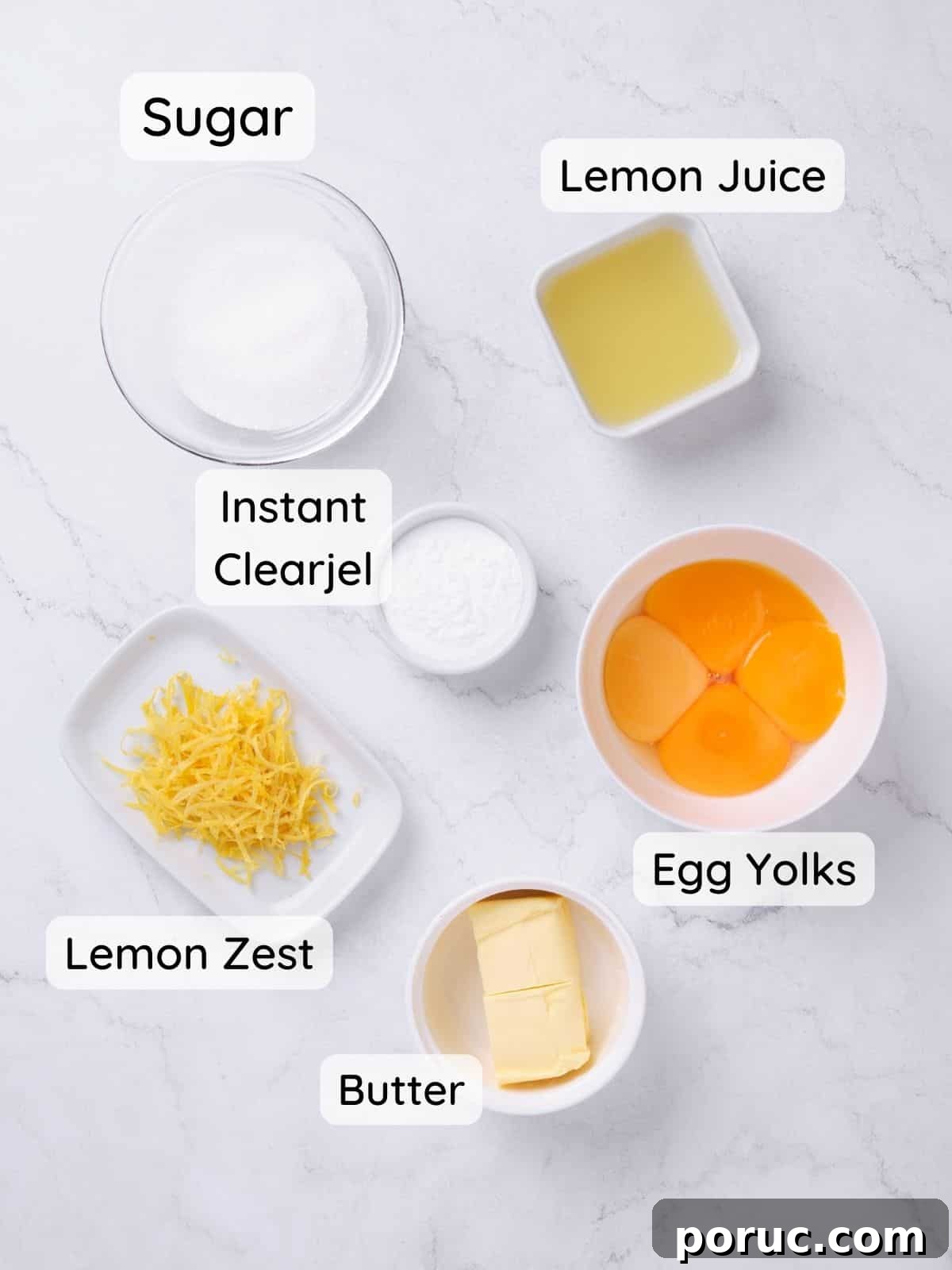 ingredients to make lemon curd cake filling on a marble surface, including sugar, instant clearjel, egg yolks, lemon juice and zest, and butter.
